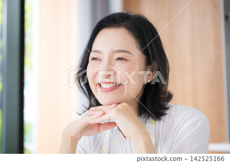 一位中年婦女的特寫鏡頭,她可能是 50 多歲的家庭主婦,穿著圍裙,在自家廚房微笑。 一位中年婦女的特寫鏡頭,她可能是 50 多歲的家庭主婦,穿著圍裙,在自家廚房微笑。 142525166