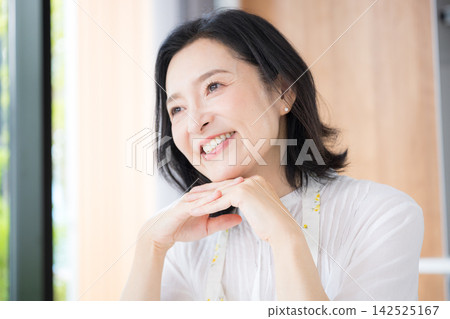 一位中年婦女的特寫鏡頭,她可能是 50 多歲的家庭主婦,穿著圍裙,在自家廚房微笑。 一位中年婦女的特寫鏡頭,她可能是 50 多歲的家庭主婦,穿著圍裙,在自家廚房微笑。 142525167