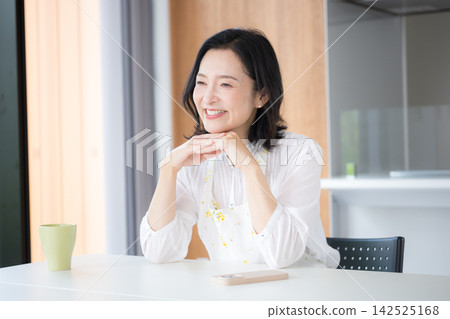 一位中年婦女，像50多歲的家庭主婦，繫著圍裙，在自家廚房微笑。 142525168