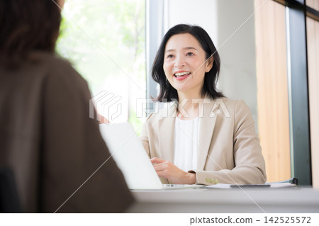 A woman in her 50s smiling and consulting with a client face-to-face; a businesswoman giving explanations and proposals in the office; communication. A woman in her 50s smiling and consulting with a client face-to-face; a businesswoman giving explanations and proposals in the office; communication. 142525572