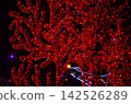 Glowing red tree branches wrapped in LED lights at night. Surreal vibrant illumination background ideal for holiday, Christmas, and night festival designs 142526289