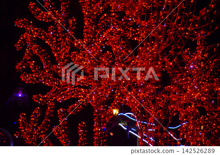 Glowing red tree branches wrapped in LED lights at night. Surreal vibrant illumination background ideal for holiday, Christmas, and night festival designs Glowing red tree branches wrapped in LED lights at night. Surreal vibrant illumination background ideal for holiday, Christmas, and night festival designs 142526289