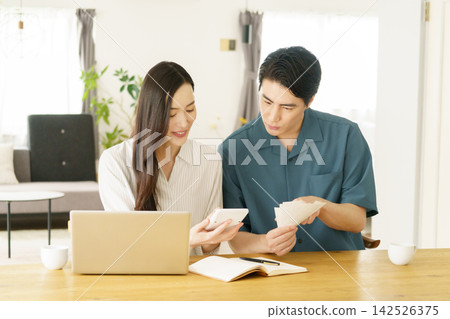 A young Japanese couple looking at receipts and a calculator at their table at home. 142526375