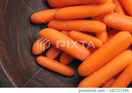 Washed peeled baby carrots served in a dark wooden bowl. Concept of healthy snack. Organic raw vegetables Washed peeled baby carrots served in a dark wooden bowl. Concept of healthy snack. Organic raw vegetables 142527266