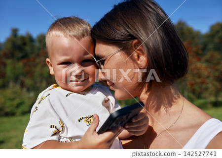 Loving mother holding smiling toddler son outdoors on sunny day Loving mother holding smiling toddler son outdoors on sunny day 142527741