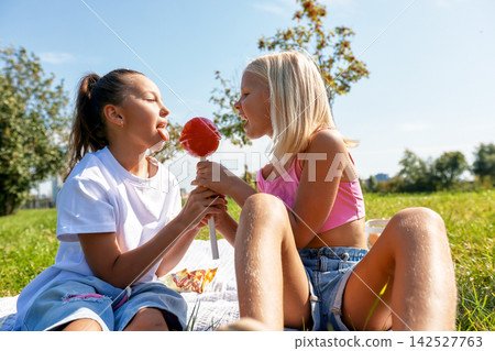 Two happy girls sharing giant red lollipop in sunny park Two happy girls sharing giant red lollipop in sunny park 142527763
