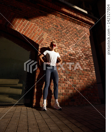 Confident athletic woman in futuristic sunglasses posing against urban brick wall Confident athletic woman in futuristic sunglasses posing against urban brick wall 142527804