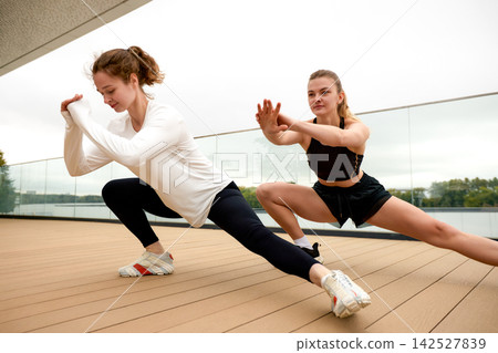 Two women doing side lunge stretch exercise on outdoor terrace 142527839