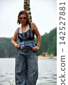 Confident woman in edgy denim and leather fashion posing by birch tree near lake 142527881