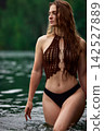 Serene woman in brown crochet bikini top wading in calm green lake 142527889