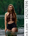 Young woman in bohemian crochet top standing in tranquil green lake 142527896
