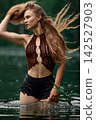 Woman in bohemian crochet top with flowing hair standing in green water 142527903