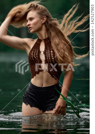 Woman in bohemian crochet top with flowing hair standing in green water 142527903