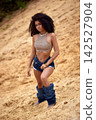 Confident young woman with curly afro hair in bohemian fashion on sandy background 142527904