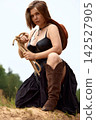 Confident woman in cowgirl attire kneeling with rope outdoors 142527905