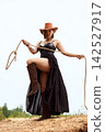 Powerful cowgirl in black dress and cowboy hat holding lasso on sandy hill 142527917