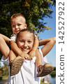 Smiling girl giving toddler brother shoulder ride outdoors on sunny day 142527922