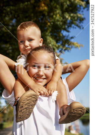 Smiling girl giving toddler brother shoulder ride outdoors on sunny day Smiling girl giving toddler brother shoulder ride outdoors on sunny day 142527922