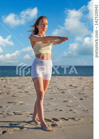 Woman holding Tadasana with stacked palms by the ocean Woman holding Tadasana with stacked palms by the ocean 142528942