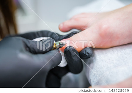 Beautician in black gloves trimming cuticles during a pedicure 142528959