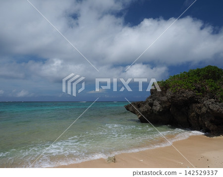 A tranquil, secluded beach with whitecaps lapping against the shore. Ikizu Beach on Ikema Island, Miyako Island, under a dynamic summer sky. A tranquil, secluded beach with whitecaps lapping against the shore. Ikizu Beach on Ikema Island, Miyako Island, under a dynamic summer sky. 142529337
