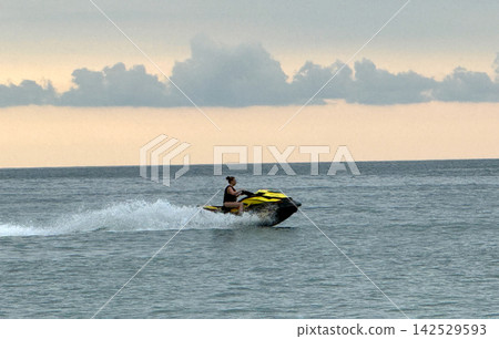 A person rides a jet ski across the water as the sun sets in the background. 142529593