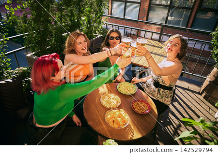 Overhead view of women toasting beer around table filled with savory snacks 142529794