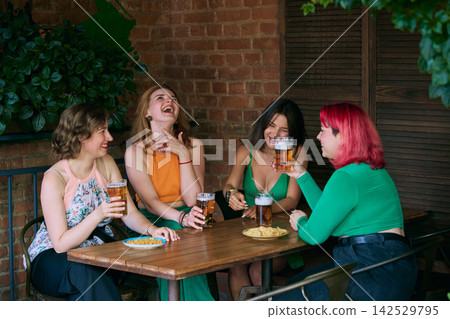 Women laugh over beer and snacks during casual gathering beside brick wall Women laugh over beer and snacks during casual gathering beside brick wall 142529795