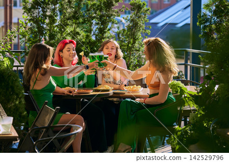 Smiling women toast with beer at lively outdoor lunch gathering in sunshine Smiling women toast with beer at lively outdoor lunch gathering in sunshine 142529796