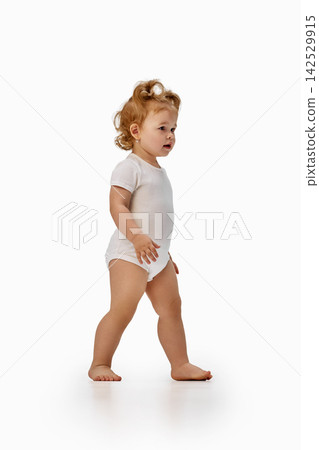 Toddler girl walking barefoot in white bodysuit. Toddler girl walking barefoot in white bodysuit. 142529915