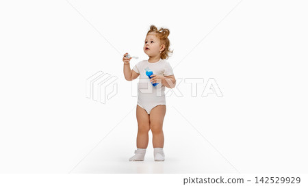Toddler girl blowing soap bubbles with blue bottle on white background Toddler girl blowing soap bubbles with blue bottle on white background 142529929
