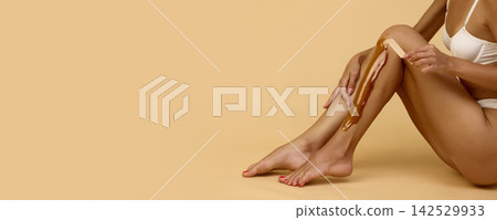 Woman applies wax to lower leg in beige beauty studio Woman applies wax to lower leg in beige beauty studio 142529933