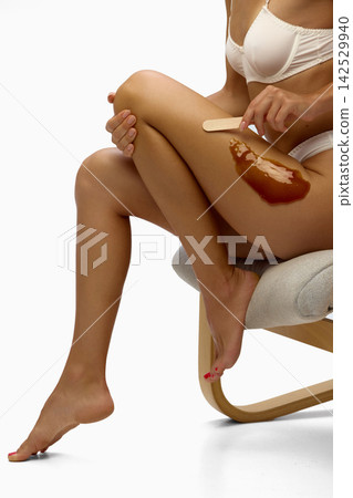 Woman applies warm wax to thigh during home epilation Woman applies warm wax to thigh during home epilation 142529940