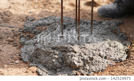 Fresh concrete fills excavated ground around rusted steel rebar, showing close up foundation work on construction site, with concrete, rebar, foundation, construction detail, showing cement 142529975