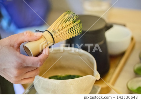 Hand holding chasen whisking matcha green tea in bowl Hand holding chasen whisking matcha green tea in bowl 142530648