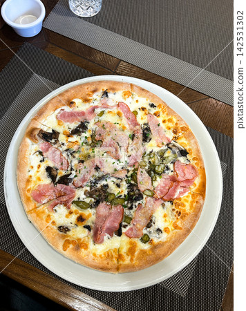 Amateur shot of pizza on restaurant table. Slightly uneven crust, melted cheese pooling. Real friendship meal without filters. Authentic evening, unpolished and warm Amateur shot of pizza on restaurant table. Slightly uneven crust, melted cheese pooling. Real friendship meal without filters. Authentic evening, unpolished and warm 142531302