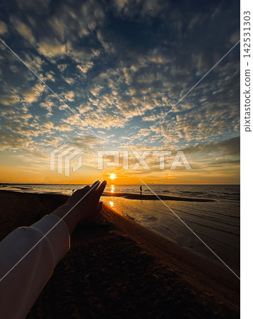 Woman reaches her hand towards sun during sunset at beach. Vertical image for tourism and travel topics Woman reaches her hand towards sun during sunset at beach. Vertical image for tourism and travel topics 142531303