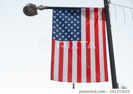 American Flag Displayed Outdoors Against Green Foliage, Patriotic United States Background American Flag Displayed Outdoors Against Green Foliage, Patriotic United States Background 142531653