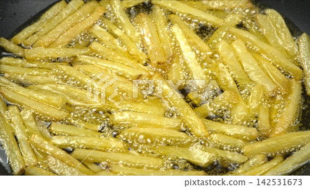 French fries sizzling and bubbling in hot golden cooking oil inside deep fryer pan, delicious crispy fast food preparation 142531673