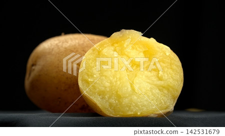 Closeup shot of boiled jacket potato cut in half revealing hot steaming fluffy yellow texture on dark background, healthy organic food 142531679