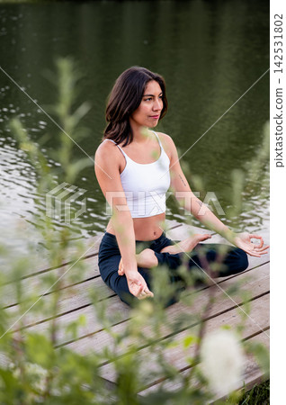 Hispanic Woman in Seated Meditation in the Park at Sunset. A young Hispanic woman practises seated meditation surrounded by greenery in a park at golden hour, connecting body and mind in nature. Hispanic Woman in Seated Meditation in the Park at Sunset. A young Hispanic woman practises seated meditation surrounded by greenery in a park at golden hour, connecting body and mind in nature. 142531802