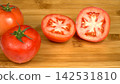 Fresh ripe red tomatoes with sliced halves arranged on bamboo wooden cutting board, organic cooking culinary ingredients 142531810