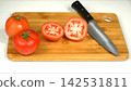 Fresh ripe red tomatoes cut in halves with chef kitchen knife on wooden cutting board, culinary cooking preparation 142531811