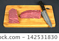 Fresh raw beef tenderloin slices arranged with professional chef knife on wooden cutting board, kitchen preparation flat lay 142531830