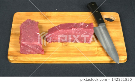 Fresh raw beef tenderloin slices arranged with professional chef knife on wooden cutting board, kitchen preparation flat lay Fresh raw beef tenderloin slices arranged with professional chef knife on wooden cutting board, kitchen preparation flat lay 142531830