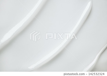 Creamy white cosmetic product spreading across smooth background, forming texture 142532324