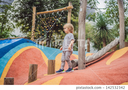 Boy climbing and balancing on outdoor playground equipment in a park with wooden posts active childhood confidence family recreation healthy movement and rear view. 142532342