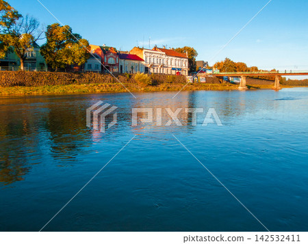 uzhhorod, ukraine - 30 aug, 2007: Uzh river in morning light. cityscape of the old european town reflecting in the water. grass embankment with trees and old architecture uzhhorod, ukraine - 30 aug, 2007: Uzh river in morning light. cityscape of the old european town reflecting in the water. grass embankment with trees and old architecture 142532411