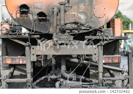 A truck equipped for asphalt application is parked on a road. The back of the truck shows pipes and machinery used for the work A truck equipped for asphalt application is parked on a road. The back of the truck shows pipes and machinery used for the work 142532482