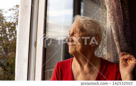 Old lonely woman sitting near the window in his house. Old lonely woman sitting near the window in his house. 142532507